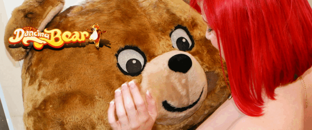 Red‑haired woman smiling and touching the large Dancing Bear mascot plush during the Dancing Bear  trial event.